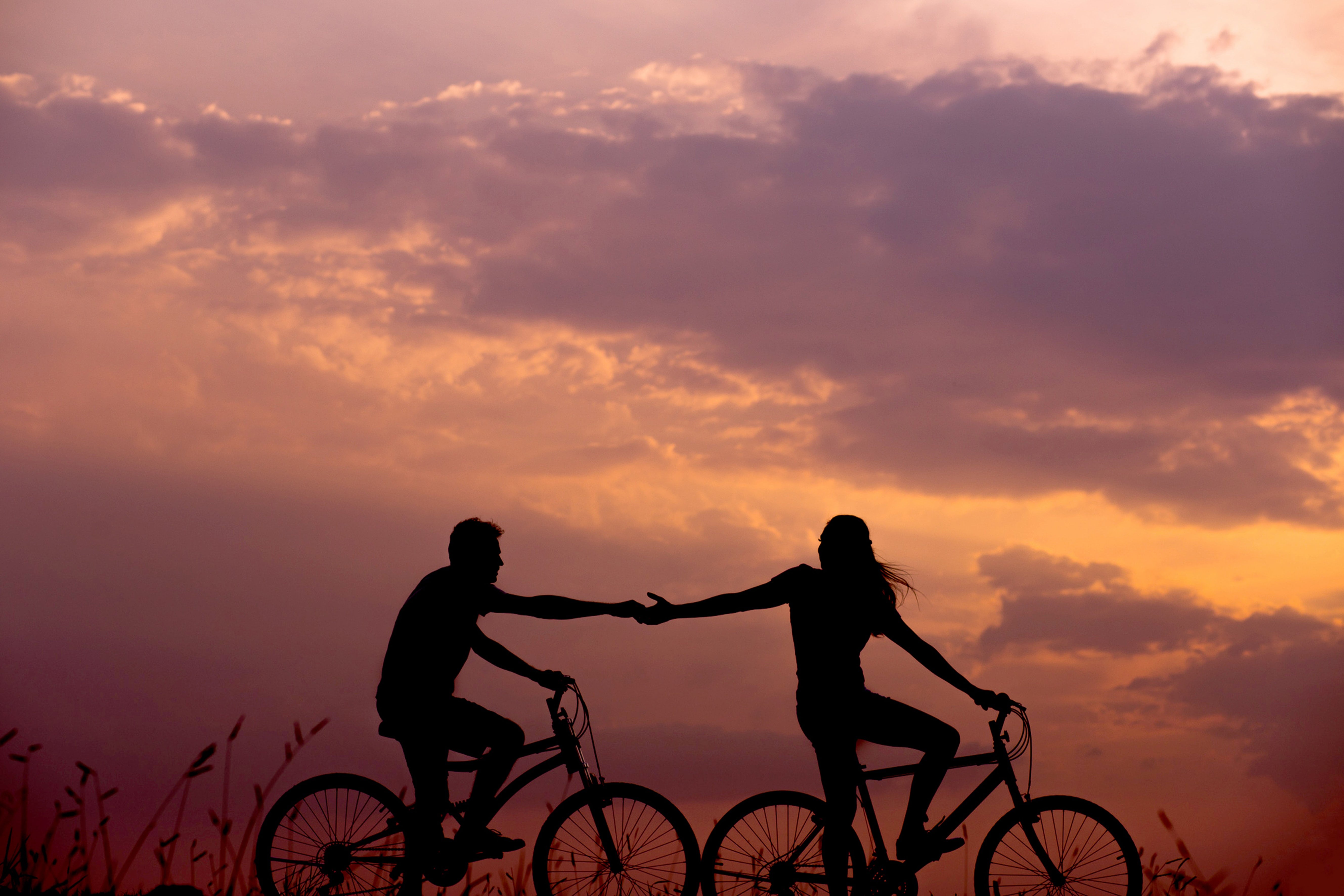 Sunset with couple holding hands while cycling