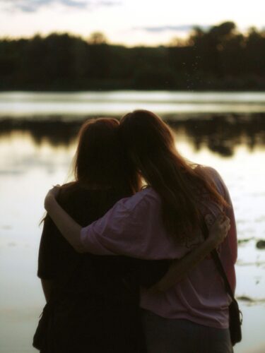 two women hugging and comforting each other by a lake